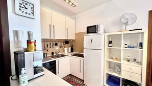 A compact kitchen with white cabinets, a microwave, a refrigerator, and a sink. There is a clock on the wall and a fan on the ceiling. - Holiday apartment modern and well equipped (Jadranovo)