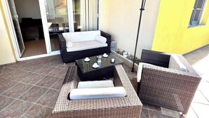 An outdoor patio area with wicker furniture, including a sofa and two chairs, a glass-top table with decorative items, and a sliding glass door leading to an interior space. - Holiday apartment modern and well equipped (Jadranovo)