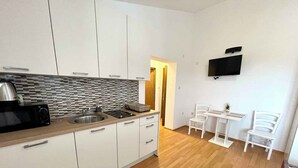 A modern kitchen with white cabinets, a stainless steel sink, and a microwave. There is a small dining area with two white chairs and a table. - Studio the sea with air conditioning (Jadranovo)