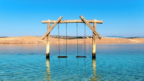A wooden swing set over clear water with a sandy beach in the background. - Studio the sea with air conditioning (Jadranovo)