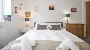 A neatly arranged bedroom with a bed, bedside tables, lamps, and framed pictures on the wall. - Wren (Weymouth)