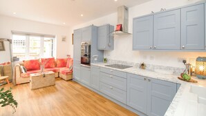 A modern kitchen with grey cabinets, a wooden dining table, and a red sofa in the living area. - Wren (Weymouth)