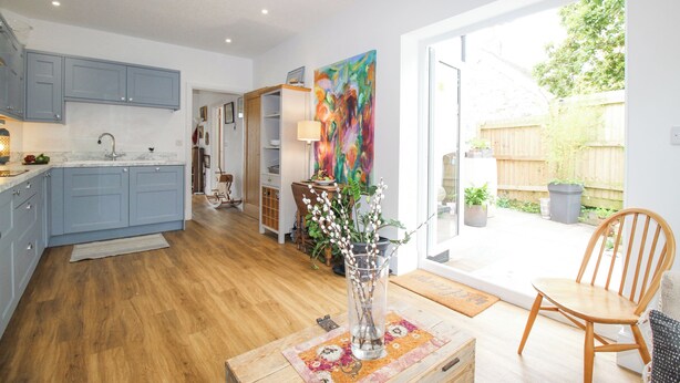 A modern kitchen with blue cabinets, a wooden dining table, and a vase with branches. - Wren (Weymouth)