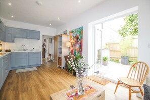 A modern kitchen with blue cabinets, a wooden dining table, and a vase with branches. - Wren (Weymouth)