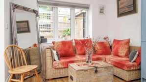A cozy living room with a wicker sofa, a wooden chair, a large mirror, and a wooden chest of drawers. - Wren (Weymouth)