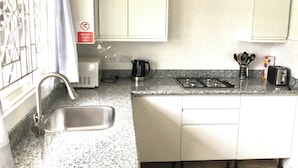 A compact kitchen with a sink, stove, and microwave. - Serenity 2-bed Apartment in Port Antonio, Portland (Port Antonio)