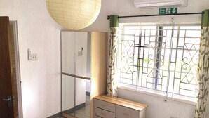 A bedroom with a bed, a wardrobe, a bedside table, a window with metal bars, and a ceiling fan. - Serenity 2-bed Apartment in Port Antonio, Portland (Port Antonio)