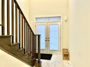 Staircase leads to a door with a glass panel, flanked by windows with blinds.