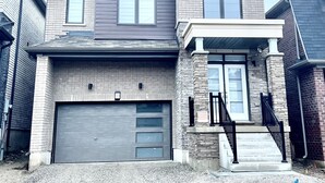 A two-story house with a garage, a front porch with a staircase, and a brick facade. - 4-Bedroom House (Caledonia)