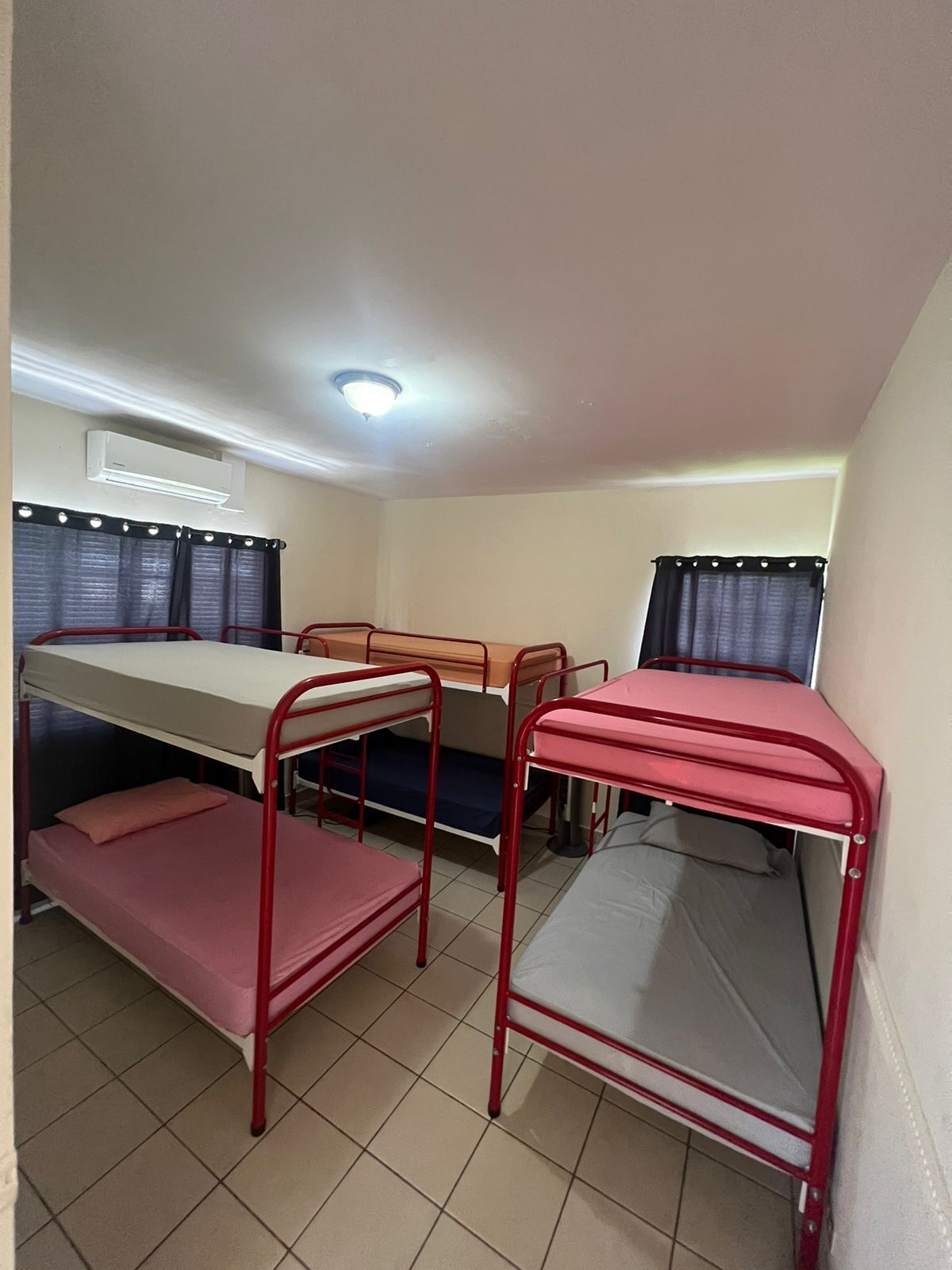 A dormitory room with bunk beds, a desk, and a window with curtains.