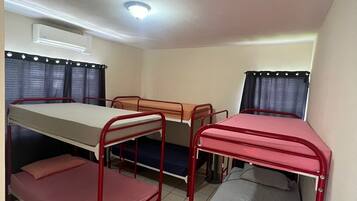 A dormitory room with bunk beds, a desk, and a window with curtains.