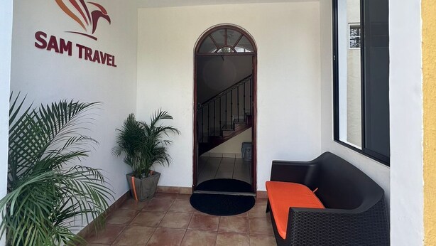 A hotel entrance with a sign reading "SAM TRAVEL," a staircase, a black wicker sofa, and potted plants. - SAM Travel Managua, Centrico de la Ciudad Capitalina (Managua)