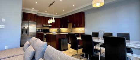 A modern kitchen with dark wood cabinets, stainless steel appliances, and pendant lighting.