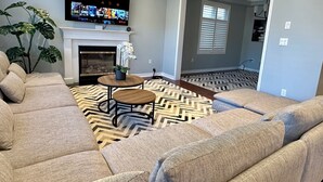 A living room with a sectional sofa, a fireplace, a TV mounted on the wall, and a patterned rug. - Cozy 5 Bedroom House in Mississauga, On  (Mississauga)