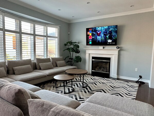 Ein Wohnzimmer mit einem Ecksofa, einem Kamin, einem Fernseher und einem gemusterten Teppich.