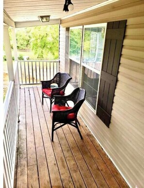 Relax on the covered porch with a table and two chairs, perfect for outdoor dining or unwinding with a view of the surrounding greenery.
