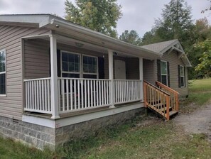 Situated in a wooded area, this cottage offers a tranquil setting with a covered porch and a small staircase leading to the entrance.