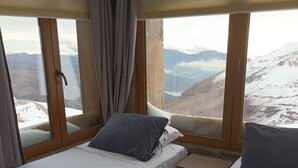 A room with two beds, a wooden nightstand, and large windows offering a mountain view. - Amplio Departamento con Vistas a la Montaña, ¡con Ski-in y Ski-out ! (Santiago)