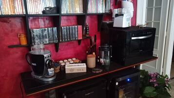 Un piano di lavoro in cucina con una macchina per caffè, un tostapane e un forno a microonde. Dietro al piano, si vedono dei libri su uno scaffale.
