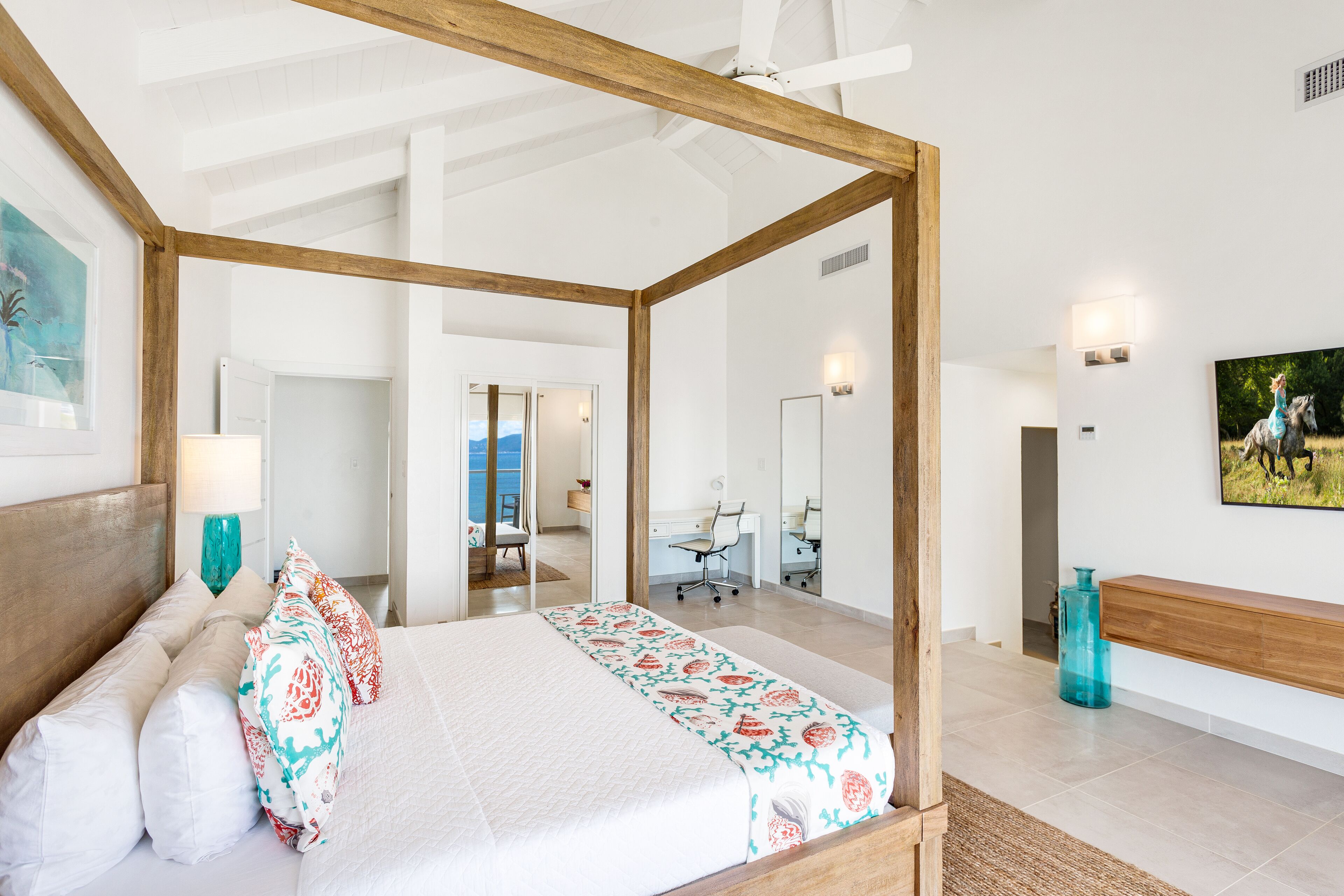 A spacious bedroom with a four-poster bed, a desk, and a large mirror.