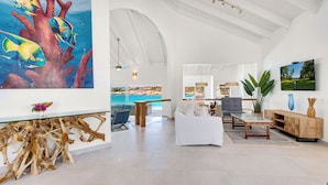 Un vaste espace de vie avec vue sur la mer, une table basse en bois, un canapé blanc et un téléviseur fixé au mur.