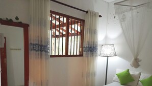 Quarto com cama, mesa de cabeceira, luminária, janela com grades e cortina.