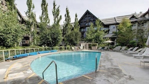 Ein Schwimmbecken mit Metallleiter, umgeben von Liegestühlen und einem Gebäude im modernen Stil.