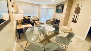 Ein modernes Wohnzimmer mit einem Glastisch, der von vier Stühlen, einem Sofa und einem Kamin umgeben ist.