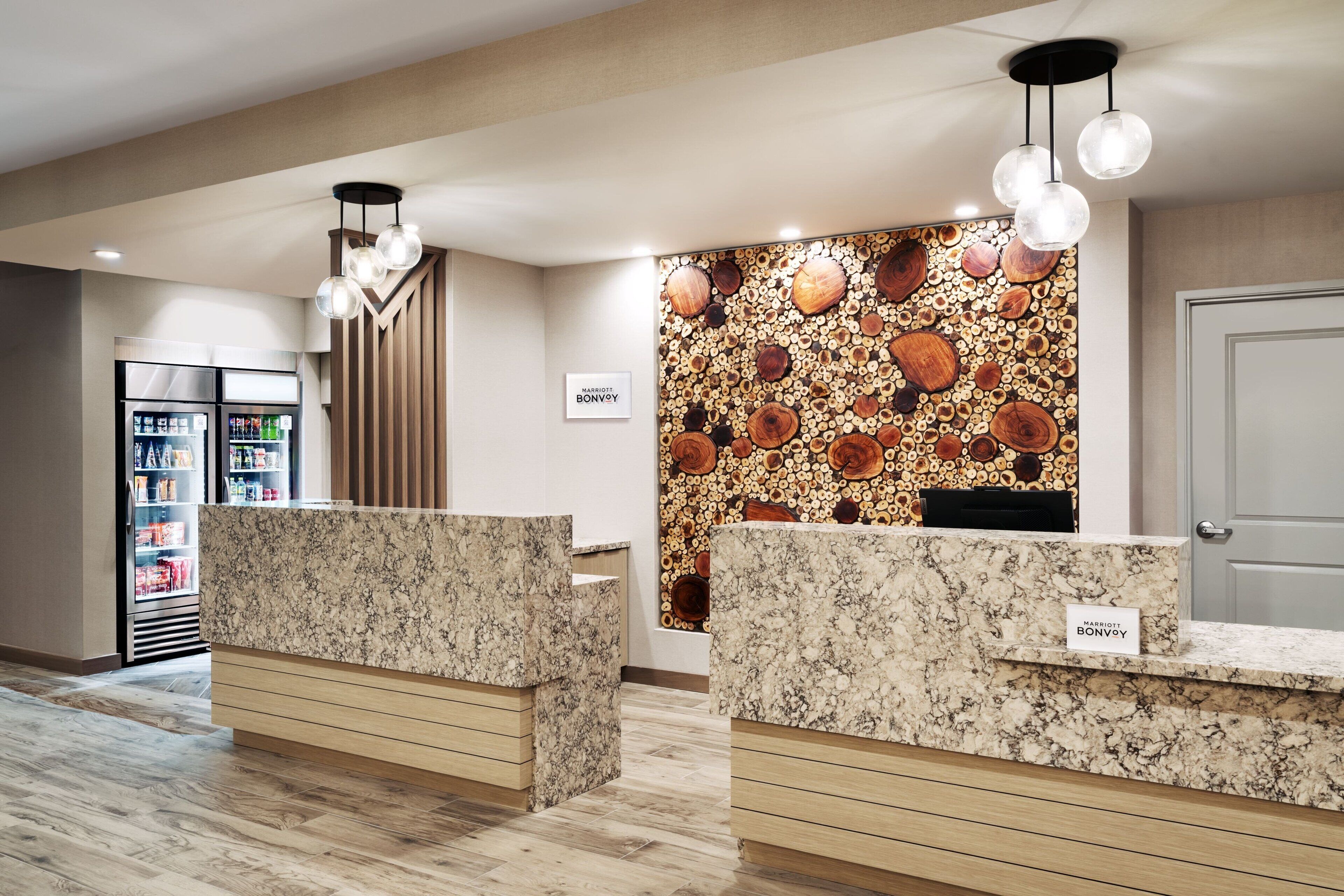 A hotel reception area with marble counters, a wall of circular wood patterns, and a minibar refrigerator.