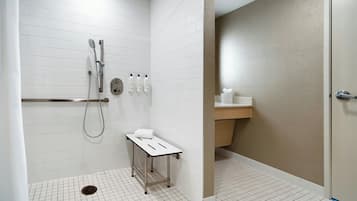 Un baño moderno con paredes de azulejos blancos, ducha con cabezal de ducha manual, una mesita con una toalla y un mostrador de madera con lavamanos.