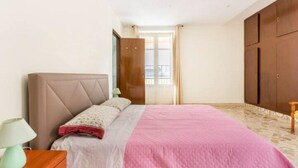 Ein Schlafzimmer mit Bett, Nachttisch, Lampe, Kleiderschrank und einem Fenster mit Vorhängen.
