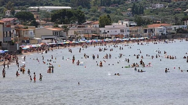 Ein voller Strand mit badenden und sonnenbadenden Menschen.