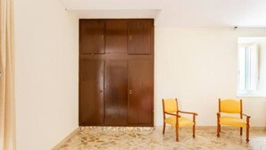 Ein Zimmer mit großem Kleiderschrank, zwei Holzstühlen, einem rosafarbenen Kissen und einem Fliesenboden.