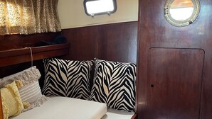 A compact cabin with a bed, zebra-patterned pillows, a small window, and a wooden door. - House Boat/Classic Yaght (Amsterdam)