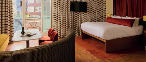 A hotel room with a bed, a TV, a table with chairs, and a view of the outside.