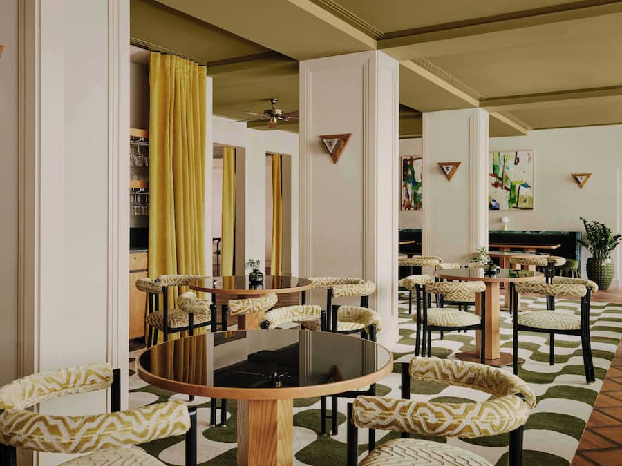 A hotel lobby with round tables, patterned chairs, a large plant, and a television.