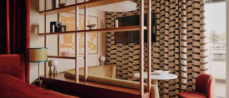 Una habitación con un sofá, una silla roja, una mesita, una lámpara y una estantería.