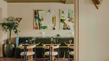 Ein Restaurantinneres mit einer grün gepolsterten Bank, drei runden Tischen mit Stühlen und abstrakten Gemälden an der Wand.