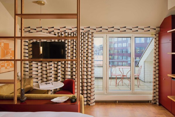 A modern room with a sofa, a small table, a TV, and a balcony with chairs. - Locke Am Platz Zurich (Zürich)