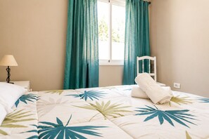 Ein Hotelzimmer mit Bett, Nachttisch, Lampe, Stuhl und einem Fenster mit Vorhängen.