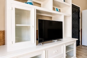 A white entertainment center with a flat-screen TV, open cabinets, and a black door in the background.