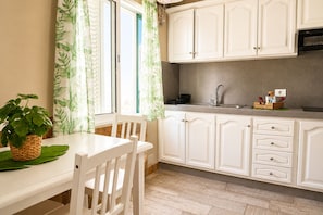 A kitchen with white cabinets, a wooden table, and a window with curtains.