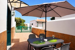 Un patio al aire libre con una mesa, sillas y un paraguas grande.