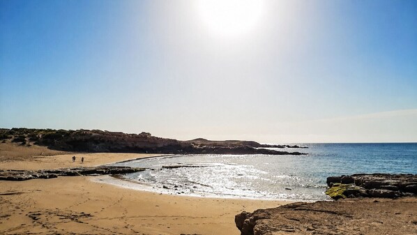 A beach with rocky formations, clear skies, and calm waters.