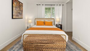 A neatly arranged bedroom with a bed, two bedside lamps, a window with curtains, a woven bench, and a painting on the wall. - Classic Inglewood Gem 3Bed/1Bath w/Jacuzzi (Inglewood)