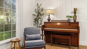 A piano with a bench, a lamp, and a plant in a room with wooden walls and a window. - Classic Inglewood Gem 3Bed/1Bath w/Jacuzzi (Inglewood)