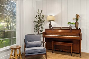 Ein Klavier mit einer Bank, eine Lampe und eine Pflanze in einem Raum mit Holzwänden und einem Fenster.