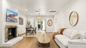 A spacious living room with a fireplace, white sofas, a coffee table, and a dining area with chairs and a table. - Classic Inglewood Gem 3Bed/1Bath w/Jacuzzi (Inglewood)