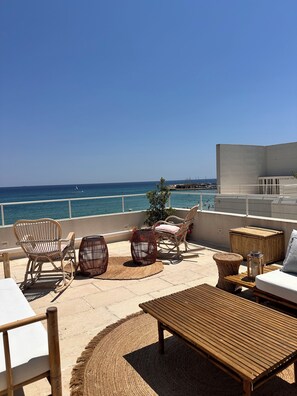 A terrace with wicker furniture, a wooden table, and a view of the sea.
