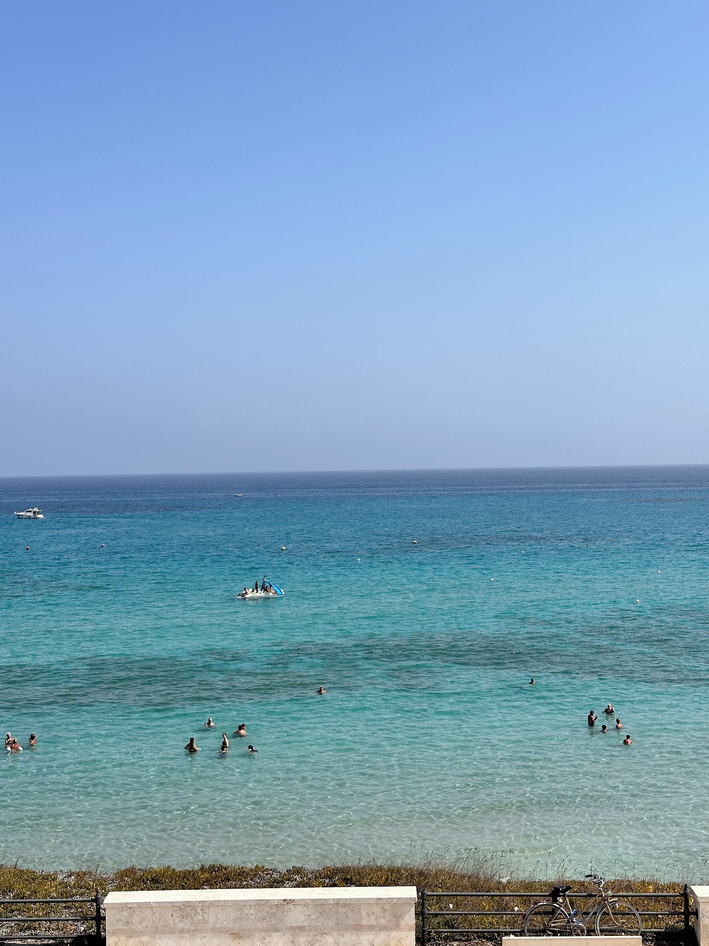 A coastal scene with clear turquoise waters, a few boats, and people swimming.